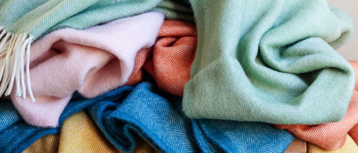 Assortment of different colour high quality Waverley Mills blankets in a pile on wooden stool.
