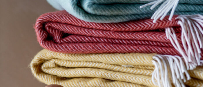 Three blankets neatly folded and stacked on top of each other. Top is blue, middle red and bottom is yellow
