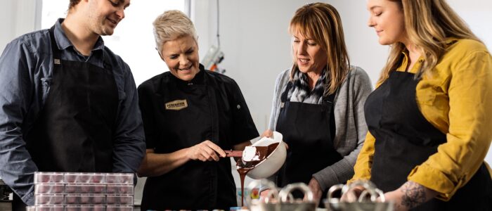 Three people stand around a woman pouring melted chocolate out of a white bowl