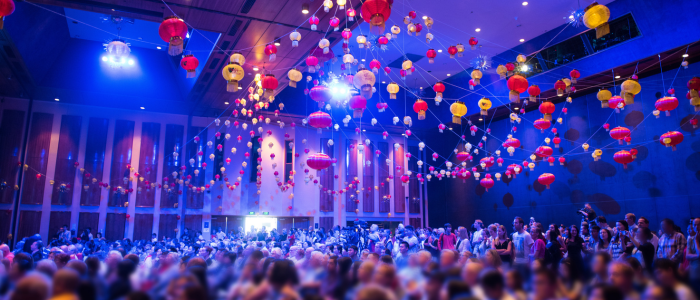 Indoor event at Wrest Point Hotel & Conference Centre with a large crowd under a ceiling decorated with colorful red, yellow, and white lanterns. Blue lighting enhances the festive atmosphere throughout the venue.