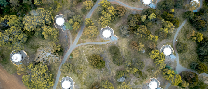 Aerial view of a natural landscape featuring multiple circular structures scattered among trees and greenery. The structures are connected by winding paths, suggesting a planned community or eco-resort integrated into the environment.