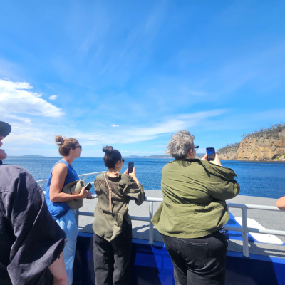 North America Famil Day 1.1 People standing on a boat deck taking photos of the ocean and distant coastline under a bright blue sky with scattered clouds.