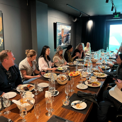 North America Famil Day 2.1 Group of people seated around a long wooden dining table in a modern, dimly lit restaurant, with plates of food, bread baskets, and glasses arranged for a shared meal.