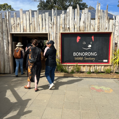 North America Famil Day 2.2 Entrance to Bonorong Wildlife Sanctuary featuring a rustic wooden facade and a large black sign with a stylized animal face and red ears, with people walking toward the doorway on a sunny day.