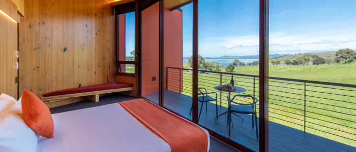 Modern cabin bedroom at Iron Creek Bay Estate with balcony and views over green fields and water.
