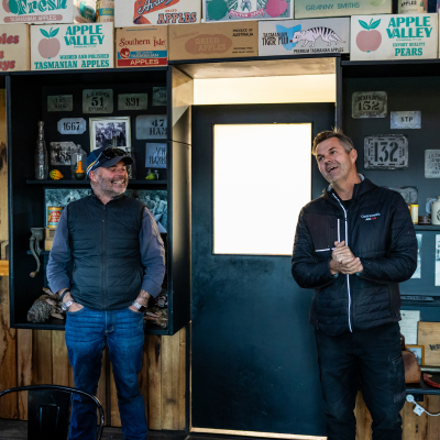 Two guides speak inside Willie Smith’s Apple Shed beneath a display of vintage Tasmanian apple crate labels.