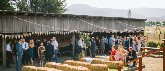 Guests gather outdoors for an event at Willie Smith’s Apple Shed, with hay bale seating, festoon decorations and mountain views.