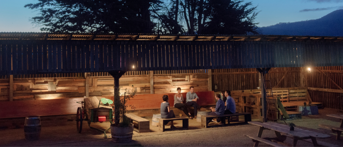Guests gather around a at Willie Smith’s rustic outdoor event space at dusk, with mountains in the background.
