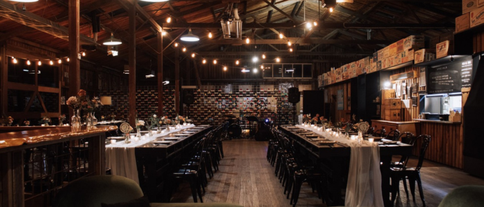 Long banquet tables are set for dinner beneath festoon lights inside Willie Smith’s rustic Apple Shed event space.
